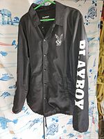 Front view of black Playboy jacket showing collar, button closure, and bunny logo on chest and right sleeve.
