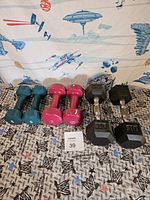 Photo showing three pairs of dumbbells in teal, pink, and black colors arranged on fabric with sci-fi themed print.
