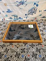 Closed wooden framed glass display case resting on patterned fabric background with Star Wars designs.