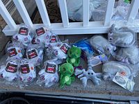 Wide view of 18 assorted plush toys on carpet including multiple white/red Domo cats, green dragon Cthulhu plushies, and gray zombie virus microbe plushies in plastic packaging.