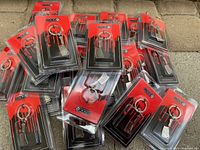 Overview of 25 individually packaged metal butcher cutter keychains, arranged loosely on a surface, showing packaging and quantity.