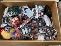 Box filled with assorted collectibles, toys, pins, patches, novelty glasses, and small toys, showing variety and packaging.