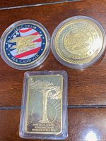 Top view of two circular Navy SEAL commemorative coins and one rectangular Last Supper gold-plated token in protective cases
