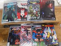 Photo showing stacks of 8 different variant comics including Black Panther, Scarlet Witch, Teenage Mutant Ninja Turtles, Aliens, Batman, Vampire Knight, Superman, Judge Dredd, each with 5 copies.