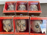 Front view of six creepy baby doll heads in their original orange and black boxes showing cracking details and blue eyes.