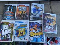 Photo showing seven Nintendo Wii video games including Dance Dance Revolution: Hottest Party; Guitar Hero III: Legends of Rock; Tiger Woods PGA Tour 07; Sonic and the Secret Rings; Just Dance 4; SpongeBob's Truth or Square; Boogie. Each game case appears complete with cover art and manuals.