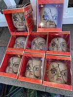 Eight cracked baby doll heads displayed out of the box; boxes present with skull patterned red design and 'Baby Doll' label