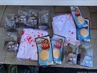 Photo showing blood splattered white cloths, multiple packages of blood soap, and boxed fake wounds arranged on a surface.