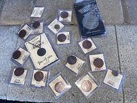 Many metal Game of Thrones coins/tokens laid out on a stone surface, some with info cards.
