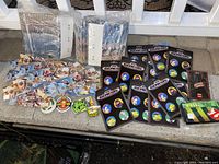 Multiple unopened packages of pinback buttons arranged on concrete floor showing Sega Genesis branded sets and other designs like Battleborn and Ghostbusters.