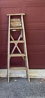Front view of 5ft wooden step ladder with four steps against a red garage door.