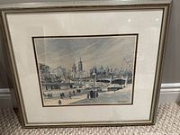 Framed print of a winter canal scene with buildings and people, displayed against a wall.