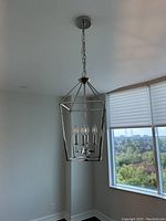 Metal frame chandelier hanging indoors by window, showing 4 candle-style lights and chain