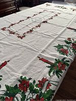 Vintage white linen Christmas tablecloth showing poinsettia, candle design and green foliage corners and border on white background.