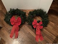 Two 20 inch green Christmas wreaths with red bows, fabric bows show signs of wear and need replacing.