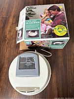 Top view of white and light grey DeVilbiss Blankscraft cool mist humidifier placed on floor next to original box.