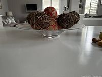 Side view of glass bowl holding ceramic and grapevine balls on a white countertop in a well-lit room