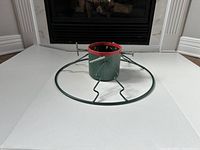 Green heavy metal Christmas tree stand with round base and four adjustable screws, shown from above and side angles.