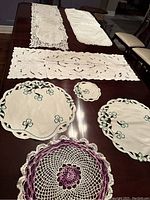 Full view of the dresser scarves and doilies displayed on a dark wood table showing patterns and colors