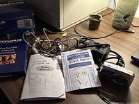 Olympus Stylus 600 digital camera with battery, charger, manuals and cables displayed on table.