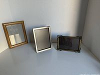 Three picture frames together on a white surface, showing a wooden 5x7 frame, a silver-tone metal 5x7 frame, and a dark metal ornate 4x6 frame.