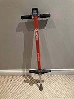 Photo of Razor branded pogo stick standing upright against a wall on carpeted floor