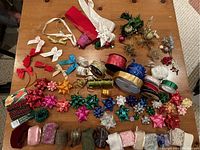 Photo showing a variety of ribbon spools, decorative bows in multiple colors, metallic ribbons, and curling ribbons on a wooden surface.