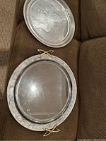 Two round metal trays shown on couch, one with gold-tone handles and one plain silver-tone