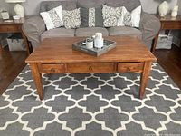 Full front view of the coffee table with three drawers in a living room setting, positioned on a patterned rug with a couch behind it.