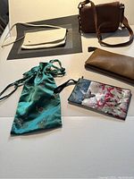 Five assorted purses including a brown leather shoulder bag, teal drawstring pouch, small floral zip pouch, beige pouch, and tan pouch on a table.