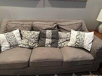 Seven decorative throw pillows arranged on a couch, showcasing various sizes and designs including white, gray, and patterned textiles.