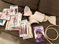 Photo showing two wooden embroidery hoops, sewing patterns, shoulder pads, and knitting book