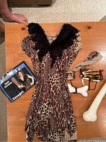 Cave girl costume dress laid flat on wooden table with bone accessories and costume packaging showing adult size.