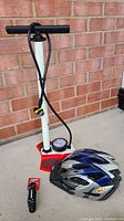 Bike pump with pressure gauge, Bell bike helmet on ground with brick wall background