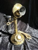 Front angle view showing brass rotary dial, black handset on holder, and connected cord.