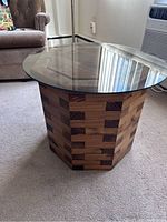 View of the hexagonal wooden stacked base and round glass top side table from an angle, showing the wood pattern and glass top reflective surface.