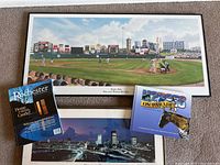 Photo of framed panoramic baseball stadium print of Frontier Field in Rochester, with a game going on, plus framed cityscape and two books including Rochester Magazine and Horses on Parade