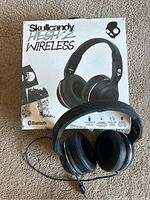 Front view of Skullcandy Hesh 2 wireless headphones with original box in background, showing product name and Bluetooth logo on box.