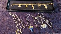 Overview of all four jewelry pieces including bracelet and three necklaces with different Jewish symbols on a fabric surface.