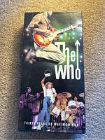 Black slipcase box showing the cover photo including band members performing live, featuring guitar, drums and energetic poses.