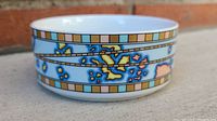 Side view of ceramic dish showing detailed vintage style map with continents in blue, yellow, green, and pink colors and geometric border.