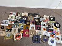 Overview photo showing large collection of vintage vinyl 45 RPM records with original sleeves laid on floor.