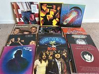 Photo showing 13 vintage vinyl LP album covers including Bruce Springsteen, Genesis, and Journey with visible wear on jackets.