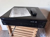 Front angled view of Yamaha CDC-675 CD player showing multi-disc tray, included remote, and user manual on top.