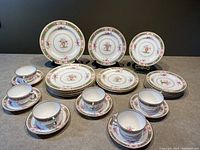 Full view showing the cups, saucers, and stacked plates with distinct floral and green bordered patterns