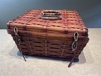Angled view of rectangular lidded wicker basket highlighting looped clasps and carved wooden pegs