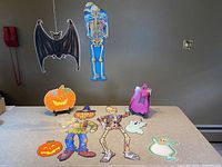 Photo of the full set of vintage cardboard Halloween decorations on a table including poseable skeletons, scarecrow, bats, pumpkins, and ghosts.