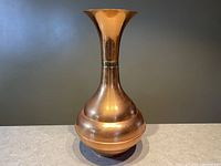 Full view of tall copper urn-shaped vase with flared opening and brass band around the neck.