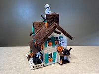 Front and side view of handmade crocheted haunted house with Halloween decorations including ghosts, black cats, and pumpkins. Roof is shown in place.