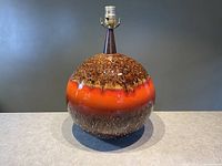 Front view of large spherical ceramic lamp base with orange and brown drip glaze finish, conical dark brown socket holder at top.
